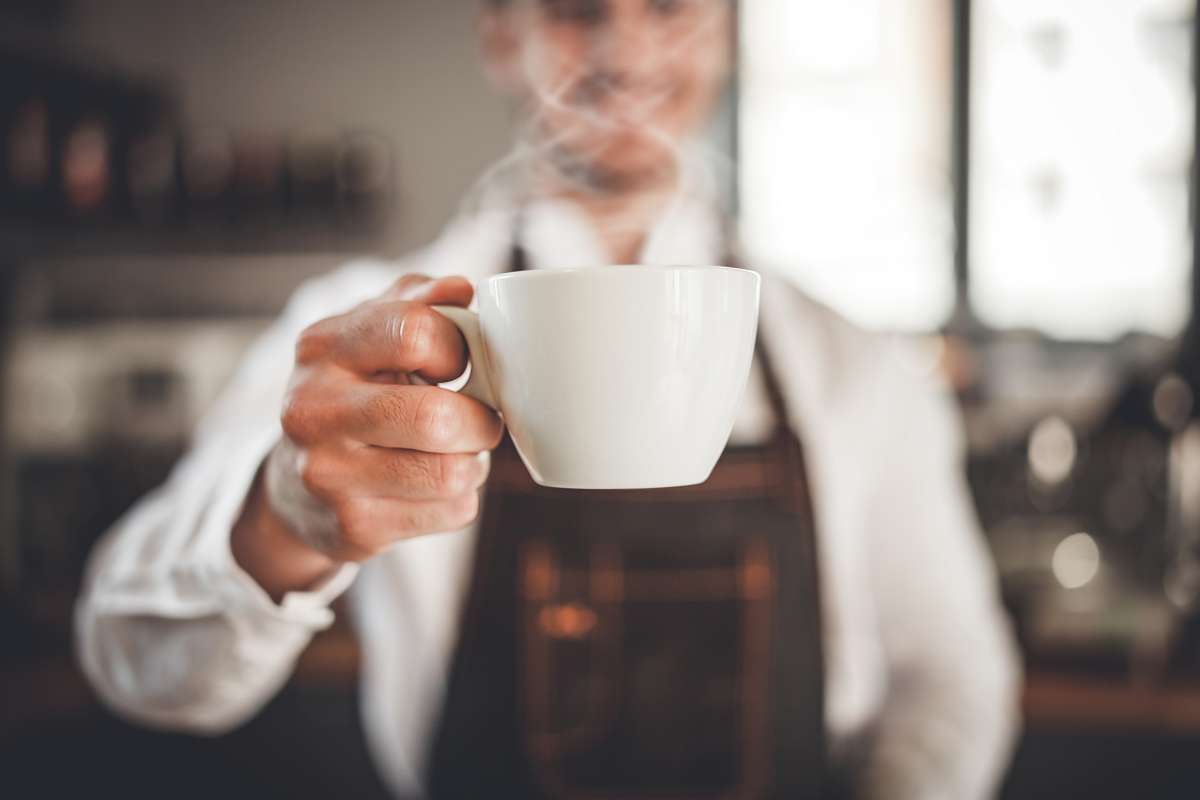 Personne versant du café dans une tasse en porcelaine blanche