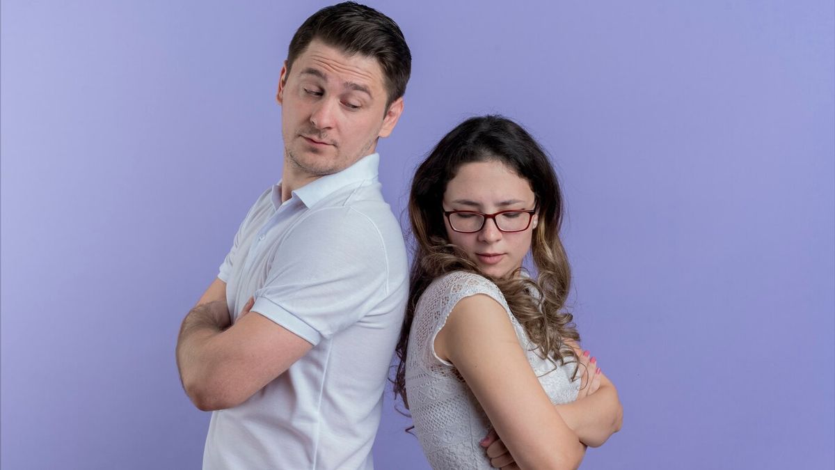 Femme regardant par la fenêtre avec expression triste, partenaire dans le flou en arrière-plan