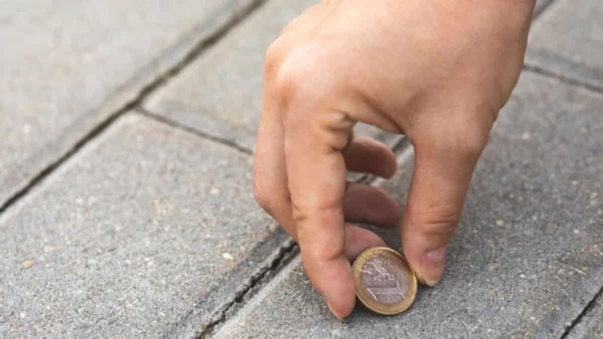 Une main ramassant une pièce de monnaie sur un sol en pierre